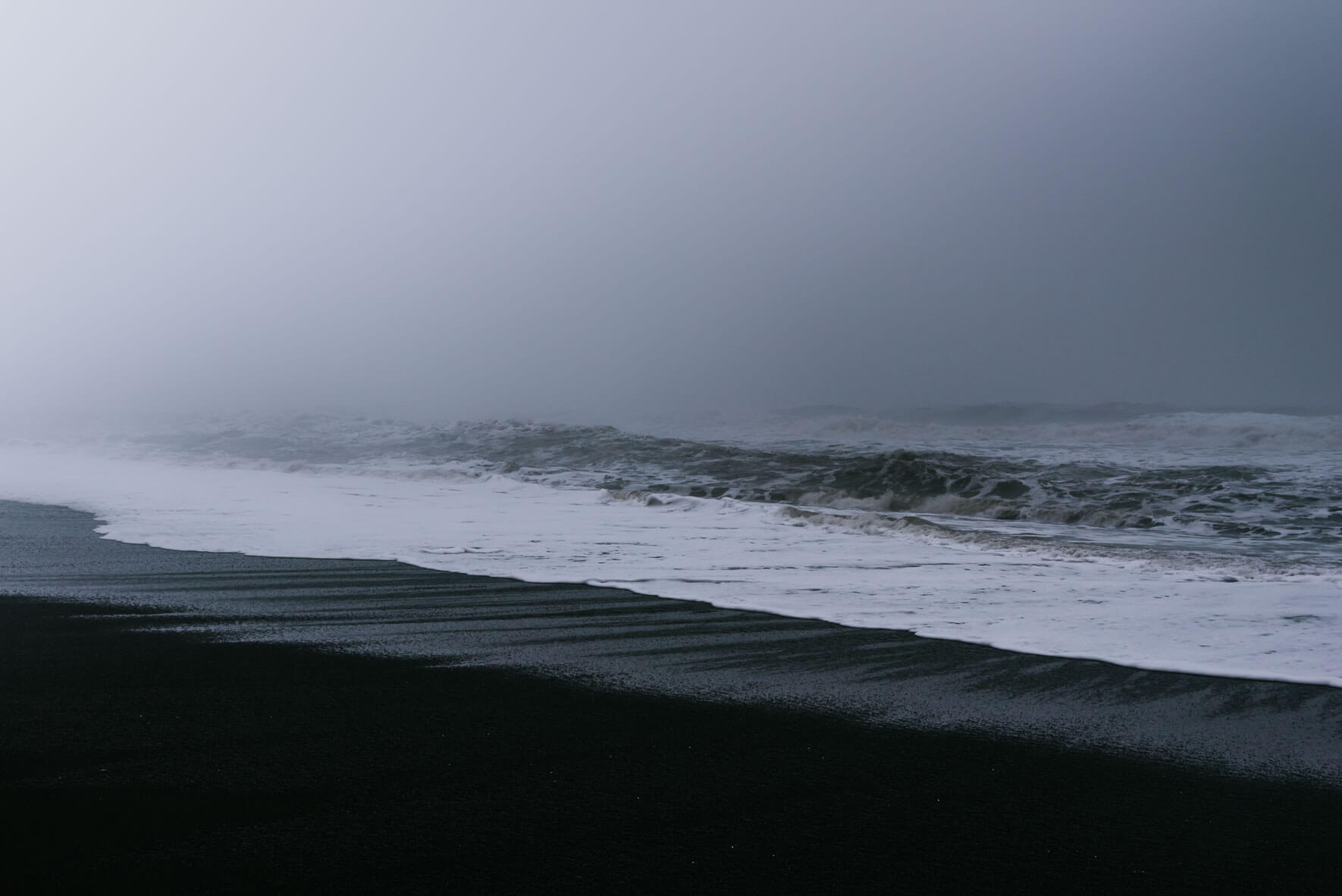 Fog and waves on black sand beach of Vík in Iceland