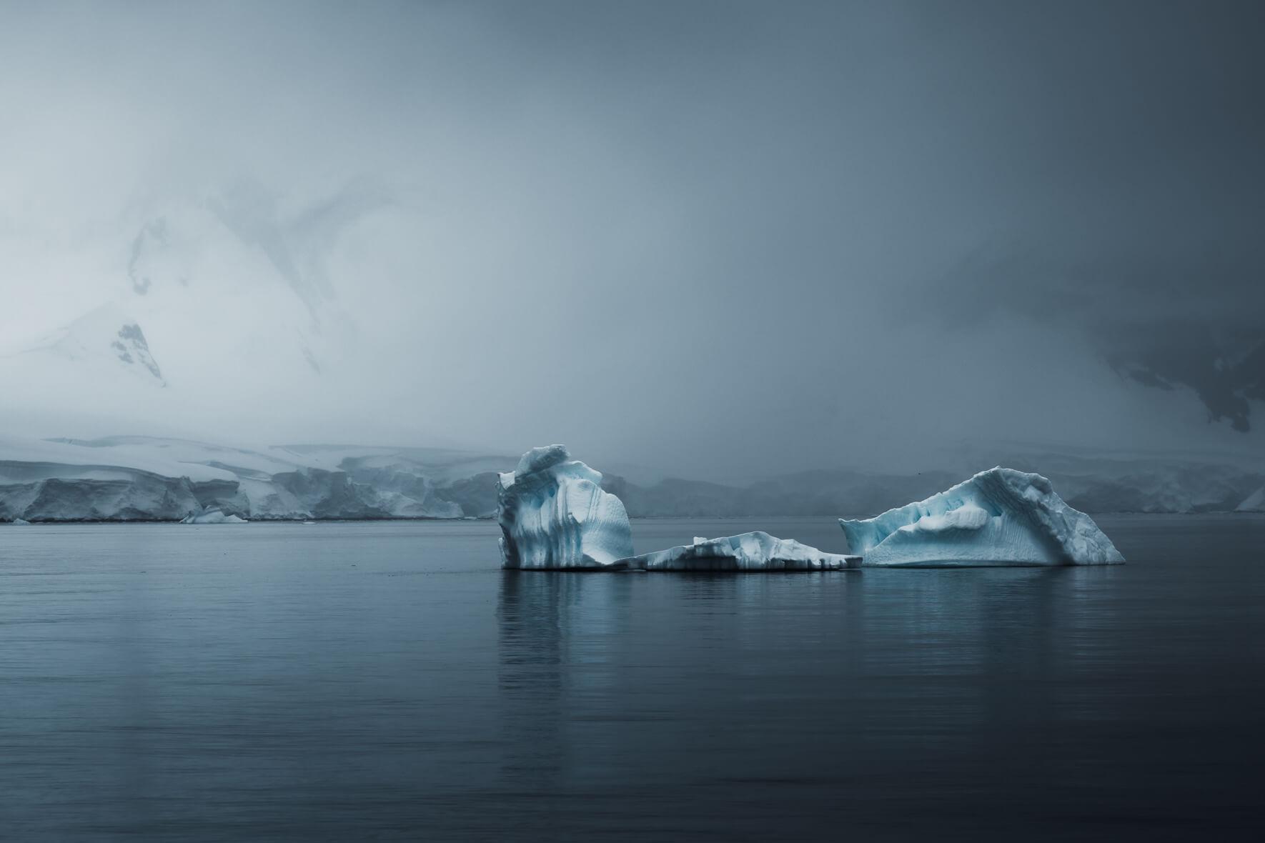 Calm scene with icebergs in dark water in Antarctica and mountains in the background