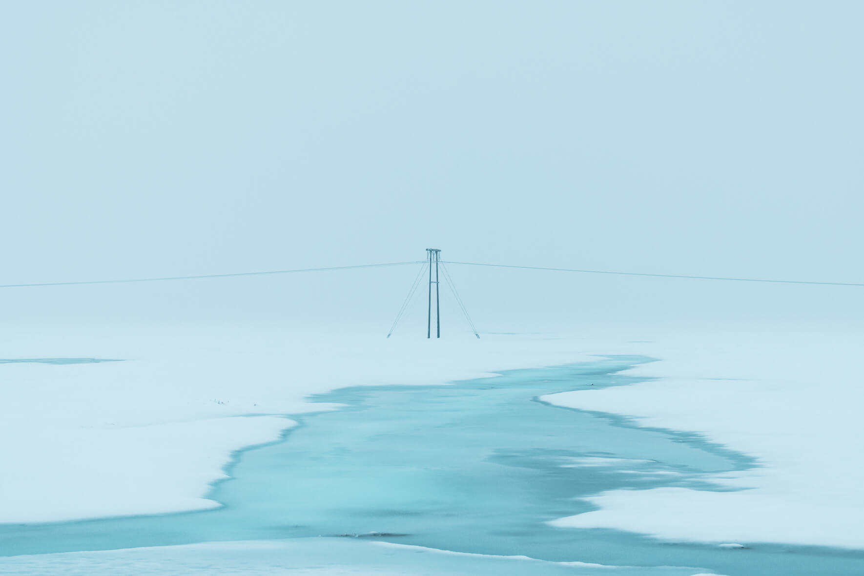Single power pole in minimalist winter landscape with frozen river in Iceland