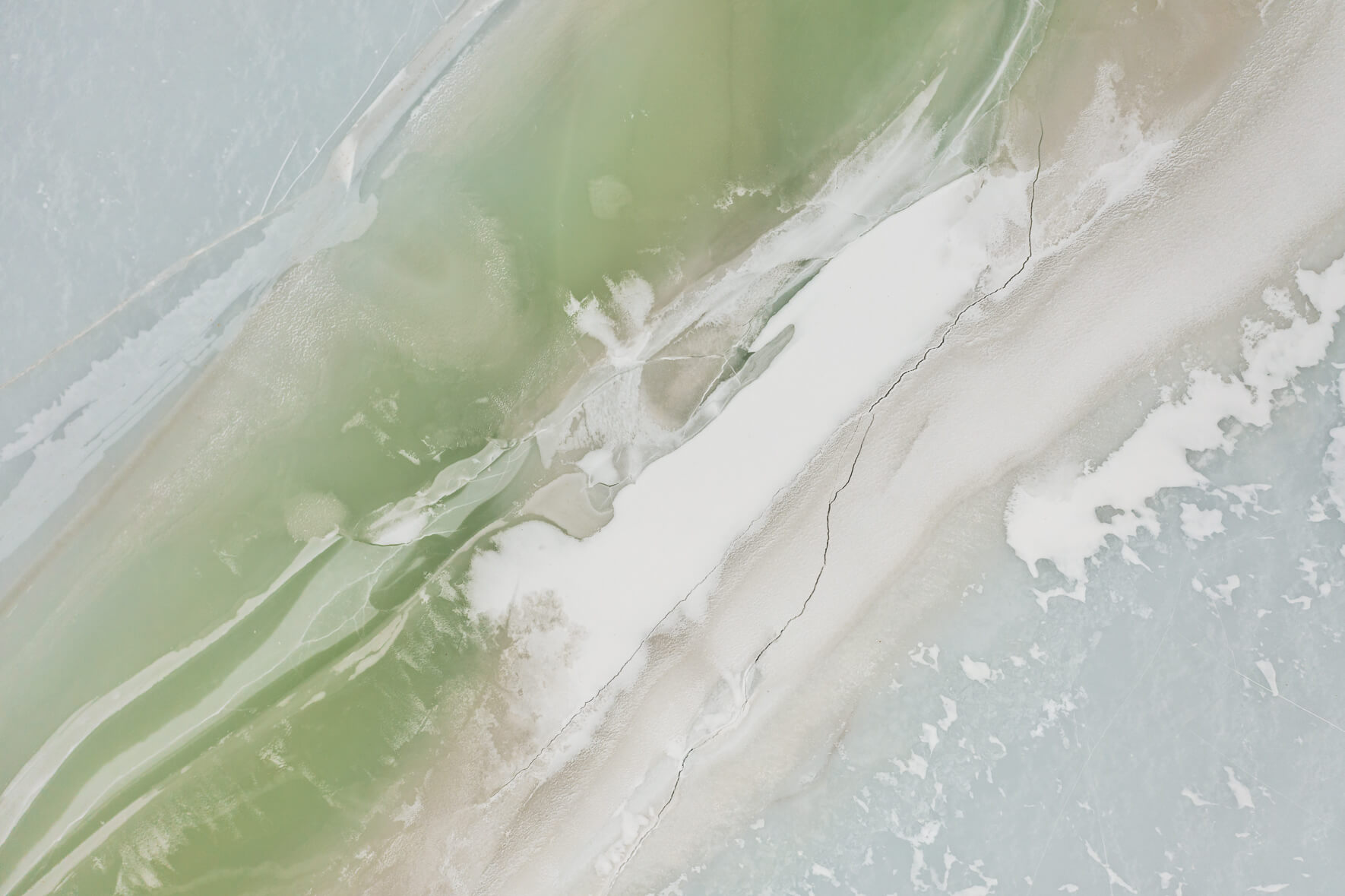 Aerial view of a frozen lake in Norway with massive cracks in the pastel colored ice surface