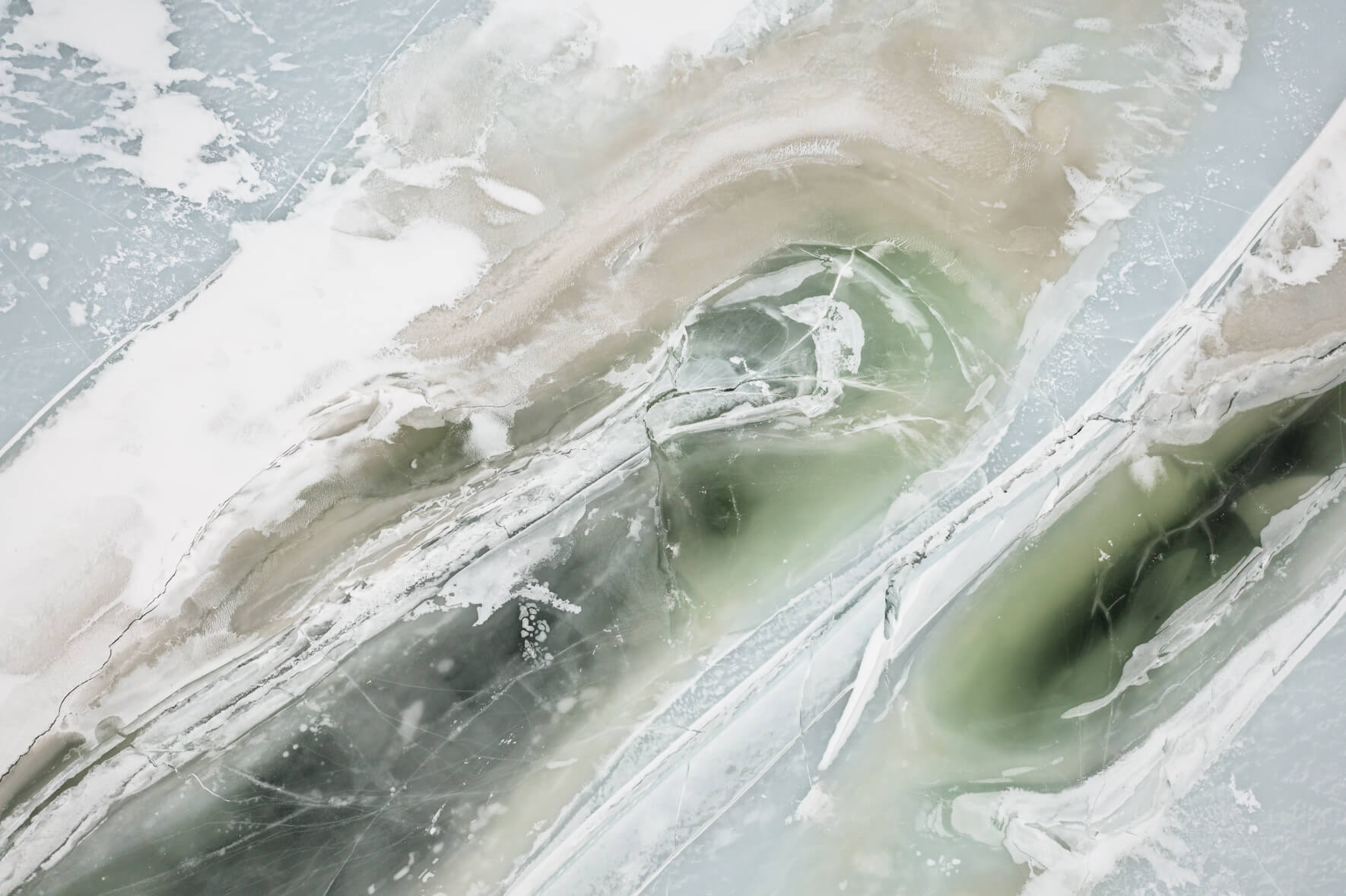 Drone view of a frozen lake in Southern Norway with massive cracks in the ice surface and colorful ice