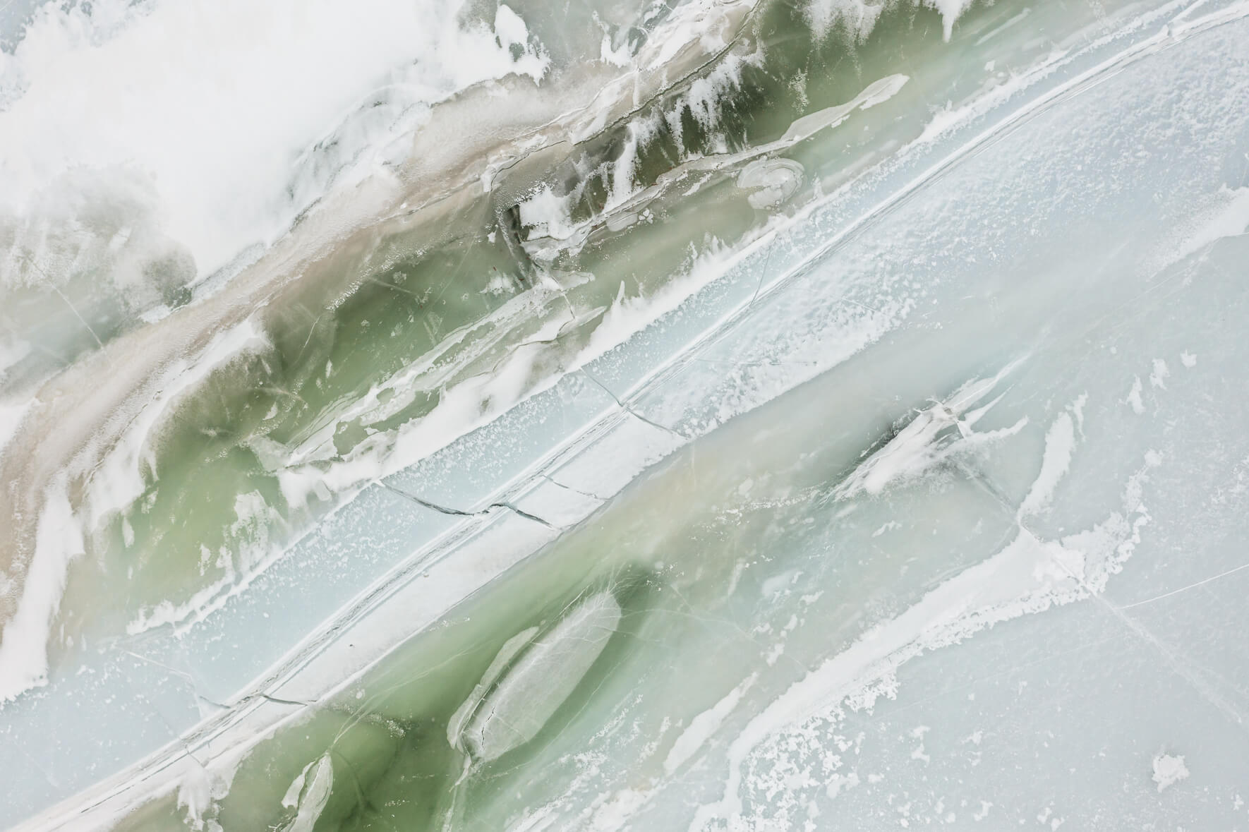 Aerial view of a frozen lake in Southern Norway with massive cracks in the ice surface and colorful ice