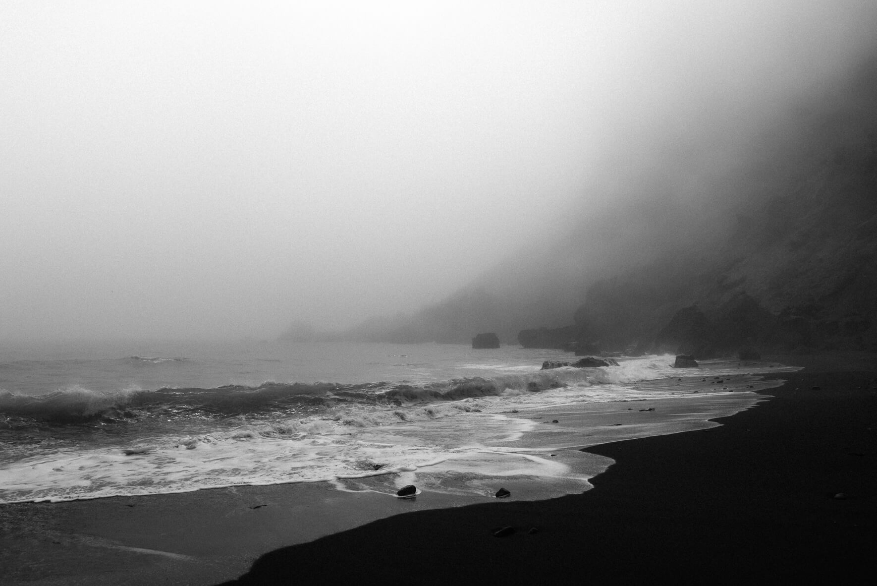 Foggy weather on the black sand beach of Vík in Iceland with waves and cliffs