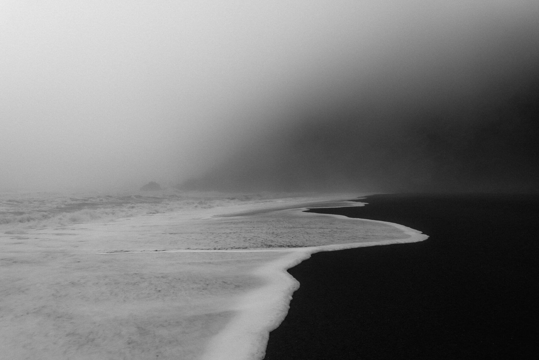 Waves on the black sandy beach of Vík í Mýrdal in Iceland with rocks shrouded in mist