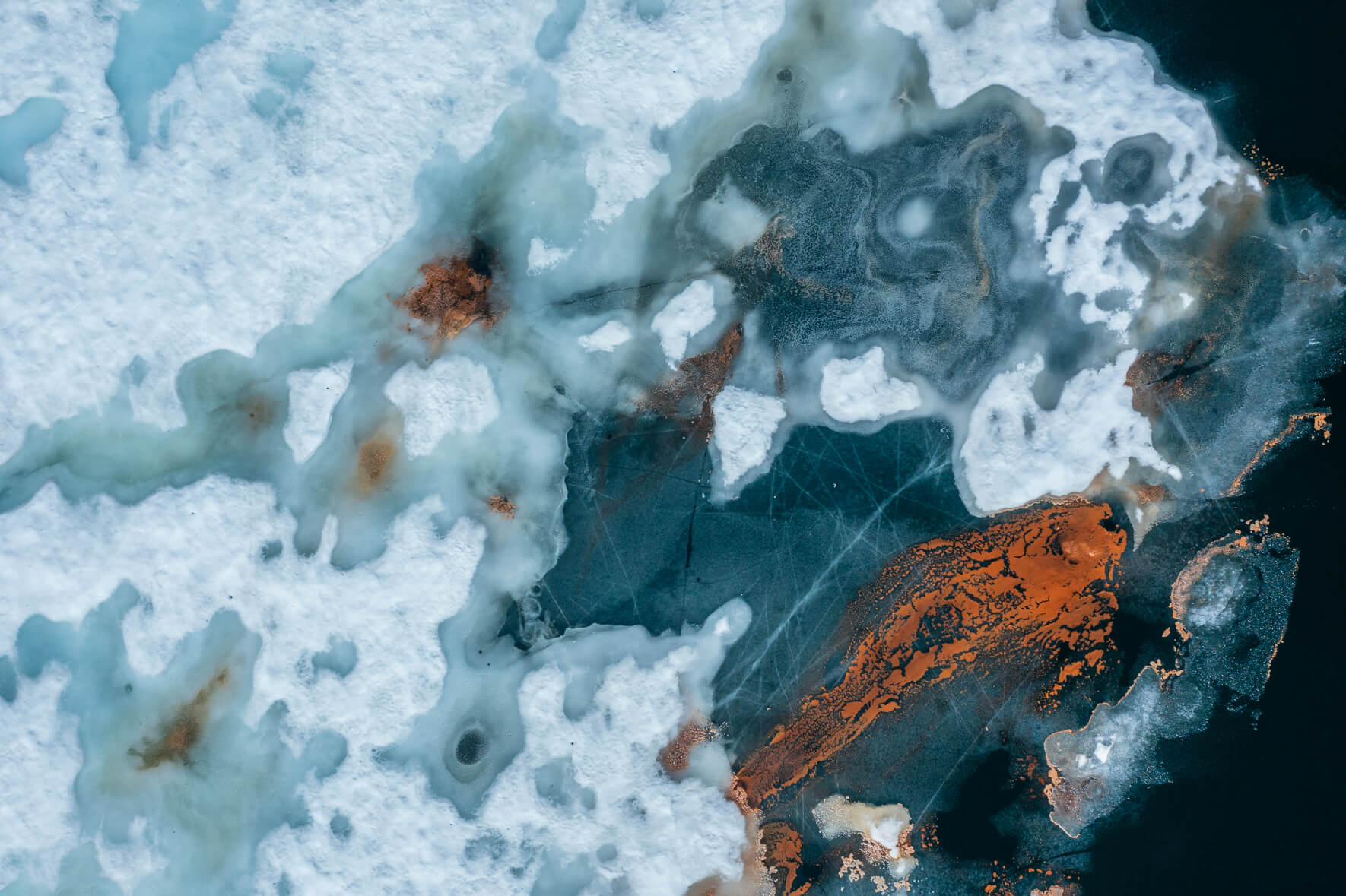 Abstract aerial view of a thawing lake in Norway with cracked ice surface and remnants of snow as well as red pollen in the shape of a fish
