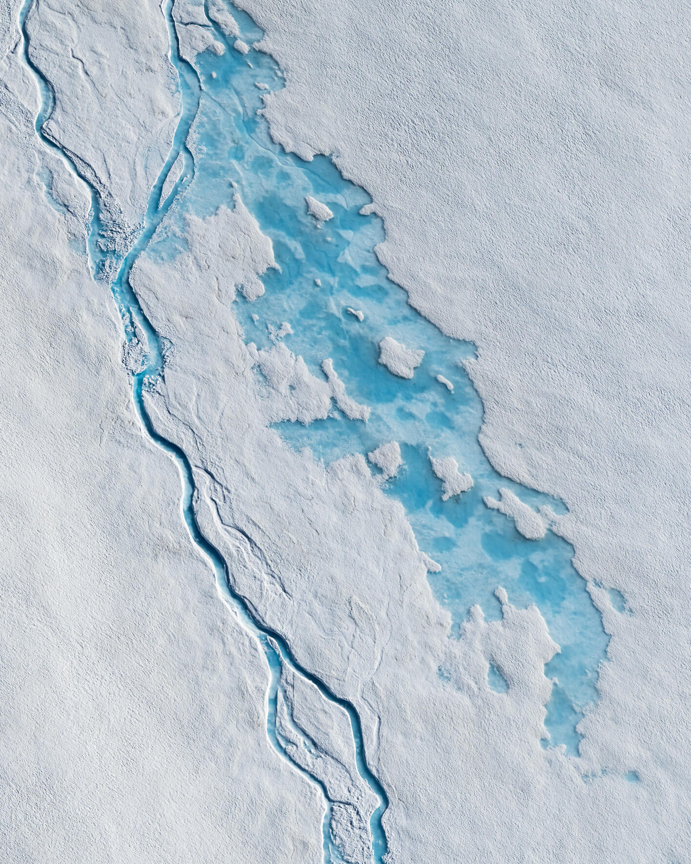 Aerial view of bright blue meltwater channel cutting through white glacier snow in Alaska