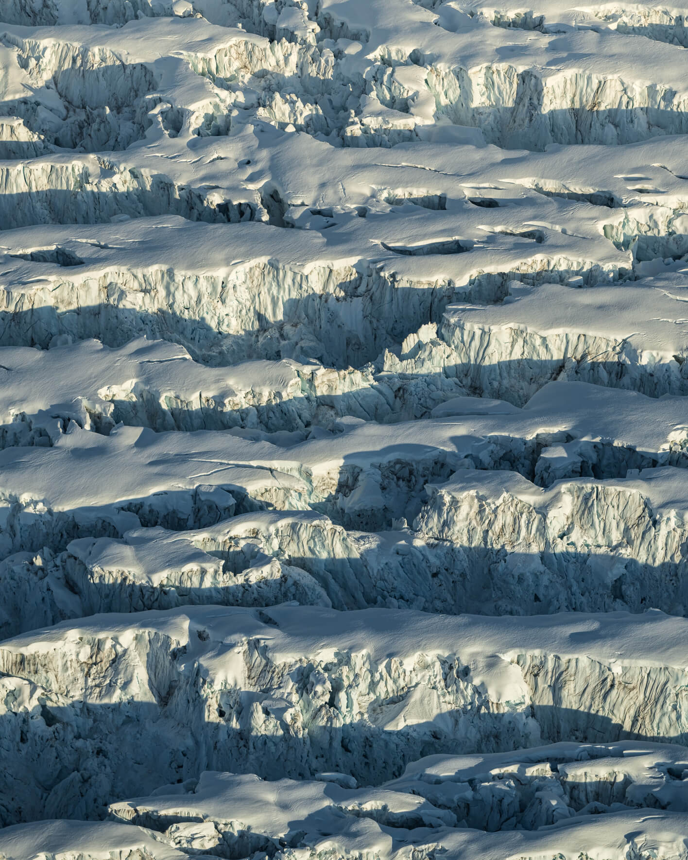 Aerial view of dark ice ridges and snow layers forming sculptural glacier patterns