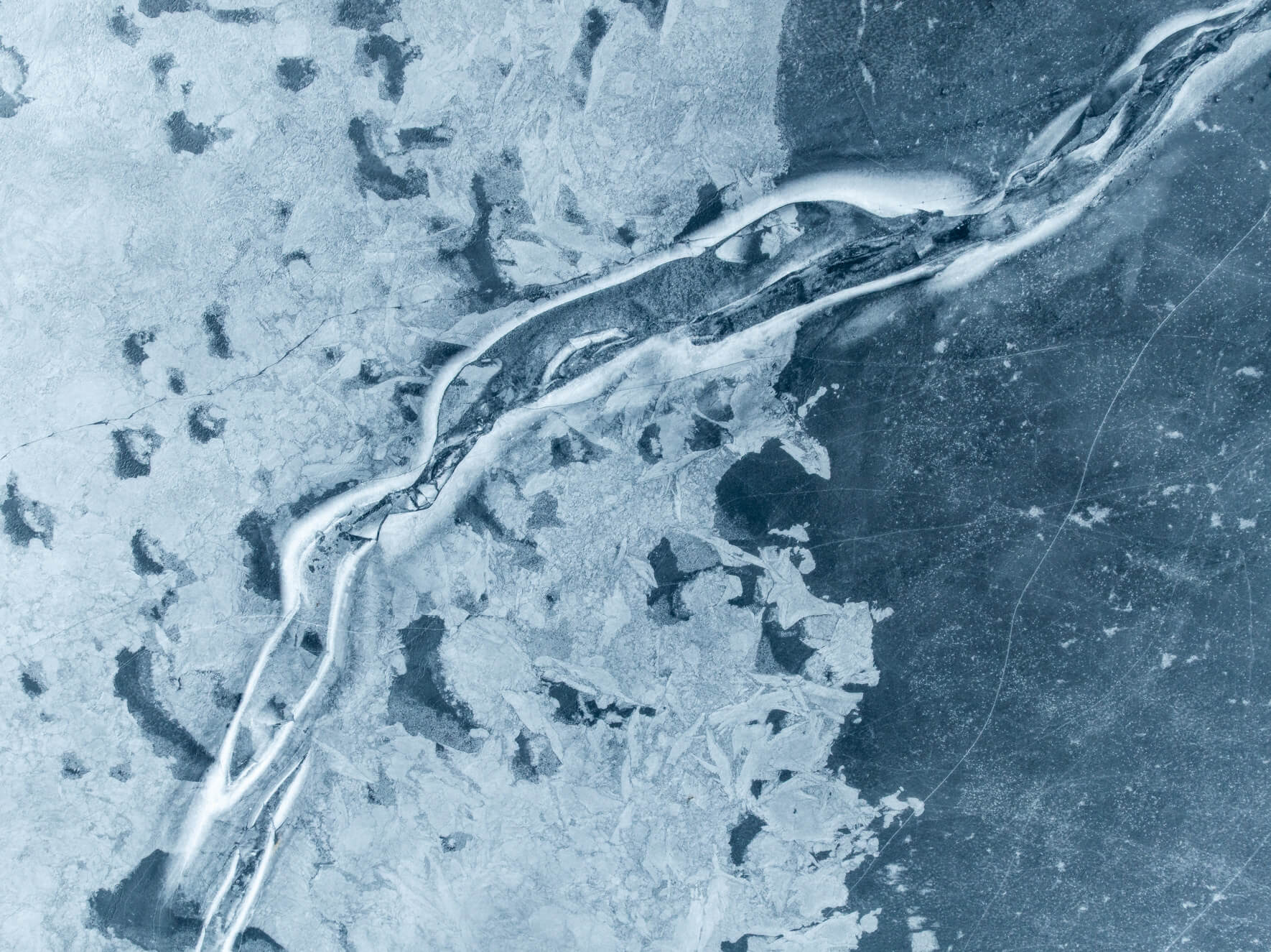 Aerial photograph of frozen lake surface with branching cracks in the ice in Norway