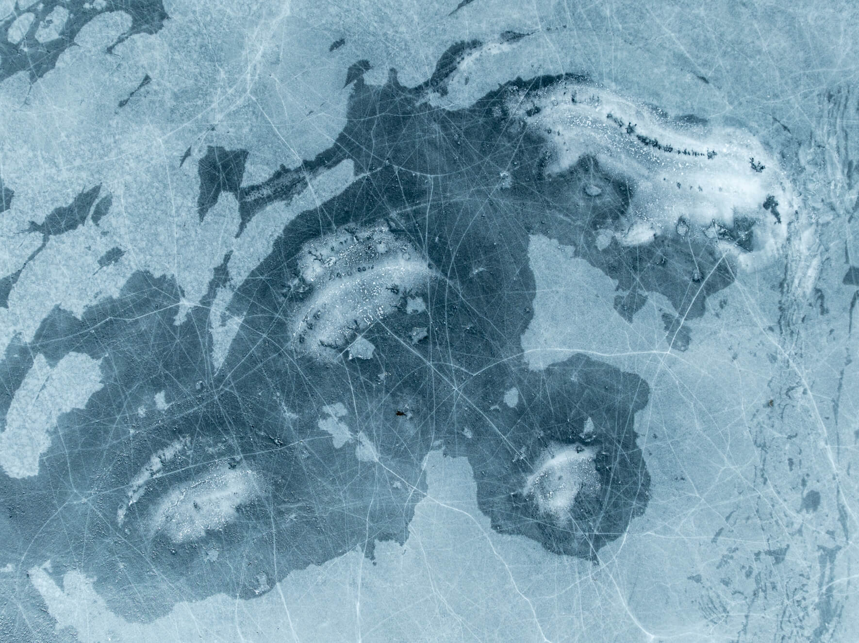 Aerial photograph of frozen lake surface with branching cracks in the ice